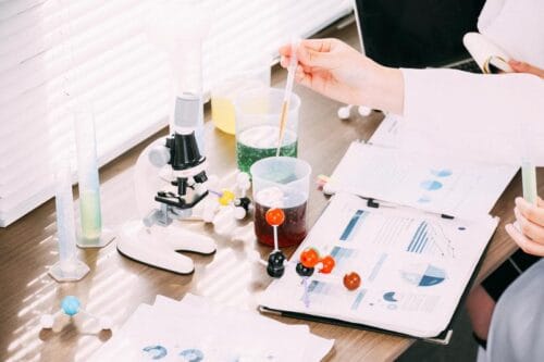 研究室の机の上で研究者がレポートを見ながら実験をする　ぱくたそ